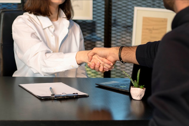 Duas pessoas apertando as mãos sobre uma mesa de reunião